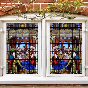 以下が含まれることがあります： テーブルの周りに集まった人々の場面を描いたステンドグラスの窓。窓は白で縁取られ、レンガの壁に設置されています。場面はカラフルで詳細に描かれており、さまざまなポーズと服装の人物が描かれています。