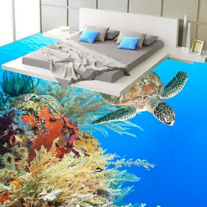 May include: A sea turtle swims over a coral reef with a bed floating above it. The bed has a gray blanket and blue pillows.