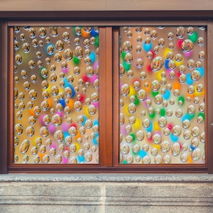 Op de afbeelding: Een raam met een kleurrijk, abstract ontwerp. Het ontwerp bestaat uit veel kleine, ronde vormen die lijken op bubbels. De bubbels zijn in een willekeurig patroon gerangschikt en zijn in verschillende kleuren, waaronder rood, blauw, groen, geel en oranje.