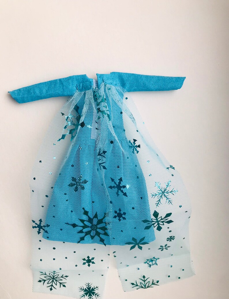 K&ouml;nnte beinhalten: Ein blaues Kleid mit einem T&uuml;ll&uuml;berzug mit Schneeflocken-Designs. Das Kleid hat lange &Auml;rmel und einen Rei&szlig;verschluss auf der R&uuml;ckseite.
