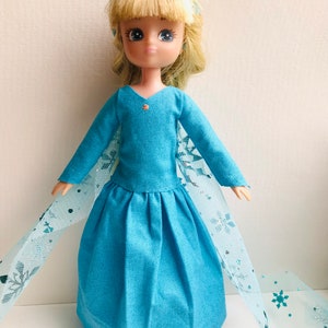 K&ouml;nnte beinhalten: Eine blaue und wei&szlig;e Puppe, die ein blaues Kleid mit Schneeflockenmuster und eine blaue Schleife im Haar tr&auml;gt.