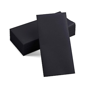 May include: A stack of black cocktail napkins with a textured diagonal pattern. Several napkins are stacked together, with one napkin slightly separated from the stack. The napkins are rectangular and appear to be made of paper.