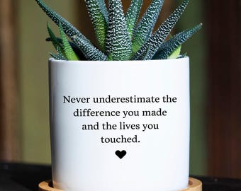 May include: A white cylindrical ceramic planter with a bamboo saucer base containing a green succulent plant. The front of the planter features the black printed text: Never underestimate the difference you made and the lives you touched, with a small heart.
