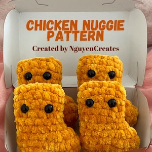 Pode incluir: Quatro peluches de nugget de frango de crochê em uma caixa de papelão marrom. Os peluches são amarelos e têm olhos pretos. A caixa tem o texto "Chicken Nugget Pattern" e "Created by NguyenCreates" impresso nela.