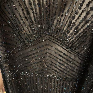 Puede incluir: Primer plano de un corpi&ntilde;o de vestido negro adornado con lentejuelas y cuentas. El dise&ntilde;o presenta patrones verticales y en zigzag, creando un efecto brillante. La tela parece ser un material oscuro y transparente.