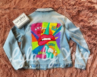 May include: A light blue denim jacket with a colorful comic book style design painted on the back. The design features a large red mouth with white teeth, and the words "BLAF!" and "BOOM!" in a colorful font.