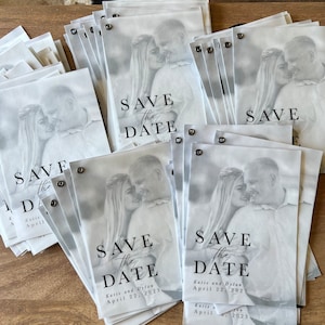 May include: A stack of save the date cards with a black and white photo of a couple. The cards are printed with the text "Save the Date" and the couple's names and wedding date.