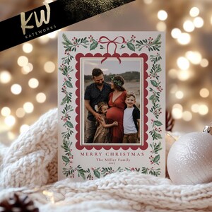 May include: A Christmas card featuring a family photo within a scalloped red frame, adorned with watercolor holly and berries. The card reads "Merry Christmas" and "The Miller Family 2023."
