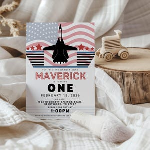 Könnte beinhalten: Eine Geburtstagseinladung mit patriotischem Thema. Das Design zeigt eine schwarze Jet-Silhouette, rote Sterne und ein amerikanisches Flaggenmotiv. Auf der Einladung steht "Maverick wird eins" mit Veranstaltungsdetails.