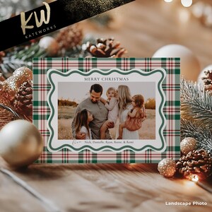 May include: Christmas card with a family photo inside a white scalloped frame. The frame is surrounded by a green and red plaid pattern. The words "MERRY CHRISTMAS" are at the top, and names are at the bottom. The card is on a wooden surface.
