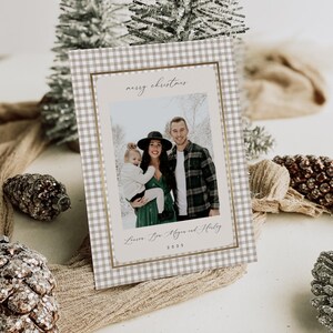 May include: A Christmas card with a family photo inside a gold-bordered frame. The card has a tan and white gingham pattern. The words "merry christmas" are at the top, and the family's names and the year 2025 are at the bottom.