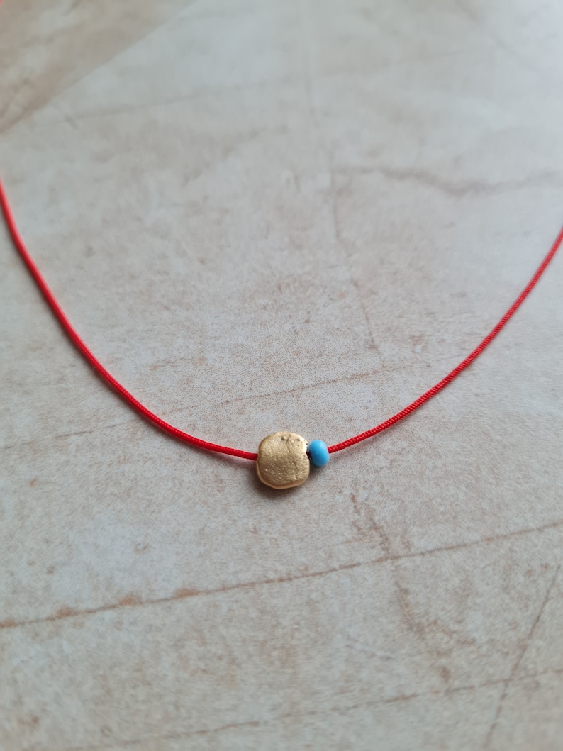 May include: A red string necklace with a gold charm and a small blue bead.