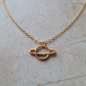 May include: A gold chain necklace with a simple gold ring pendant that resembles a planet with a ring around it.