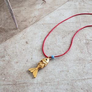 May include: A gold fish charm necklace with a blue bead on a red cord.
