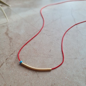 May include: A red string necklace with a gold bar pendant and a turquoise bead.