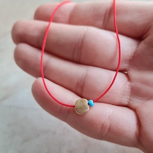 May include: A red string bracelet with a gold charm and a turquoise bead.