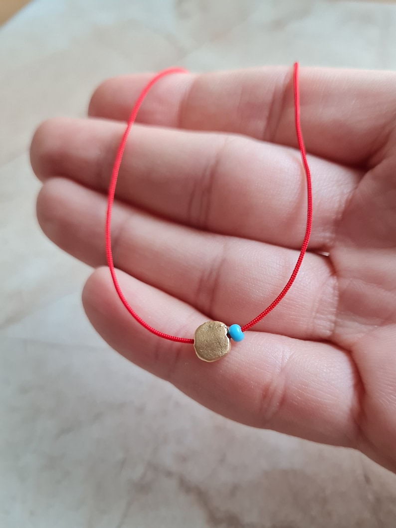 May include: A red string bracelet with a gold charm and a turquoise bead.