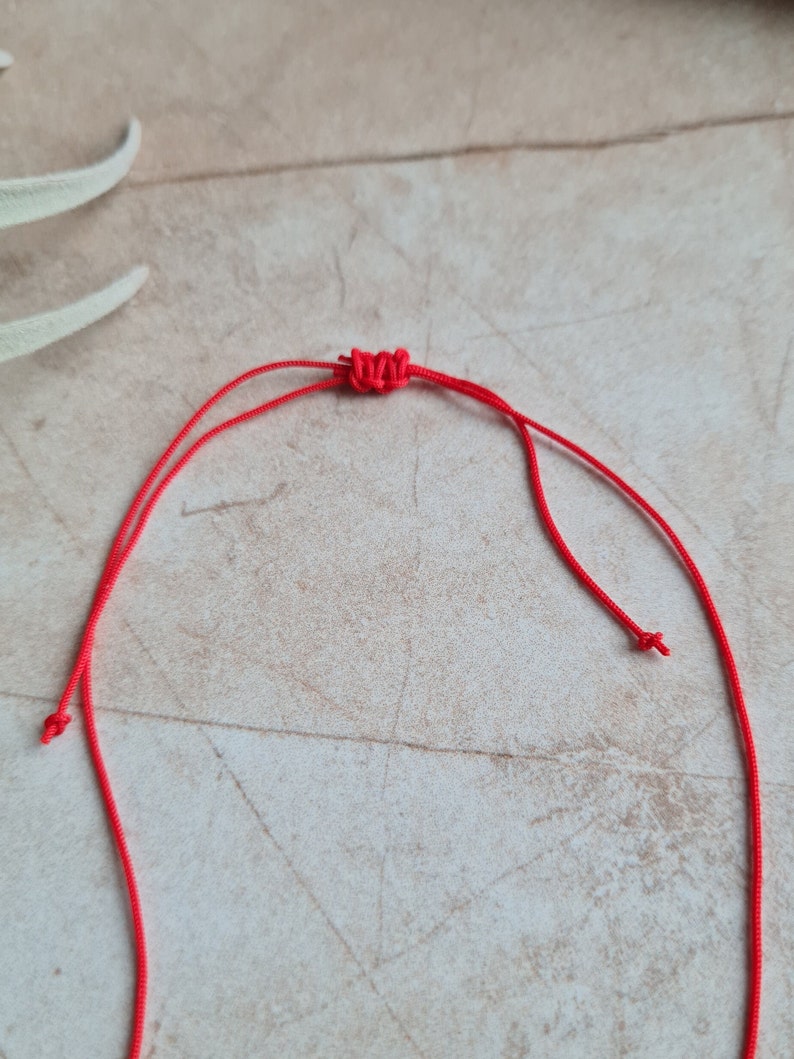 May include: A close-up of a red cord tied in a knot. The cord is on a light brown surface.