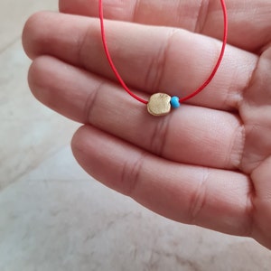 May include: A red string necklace with a gold charm and a blue bead.