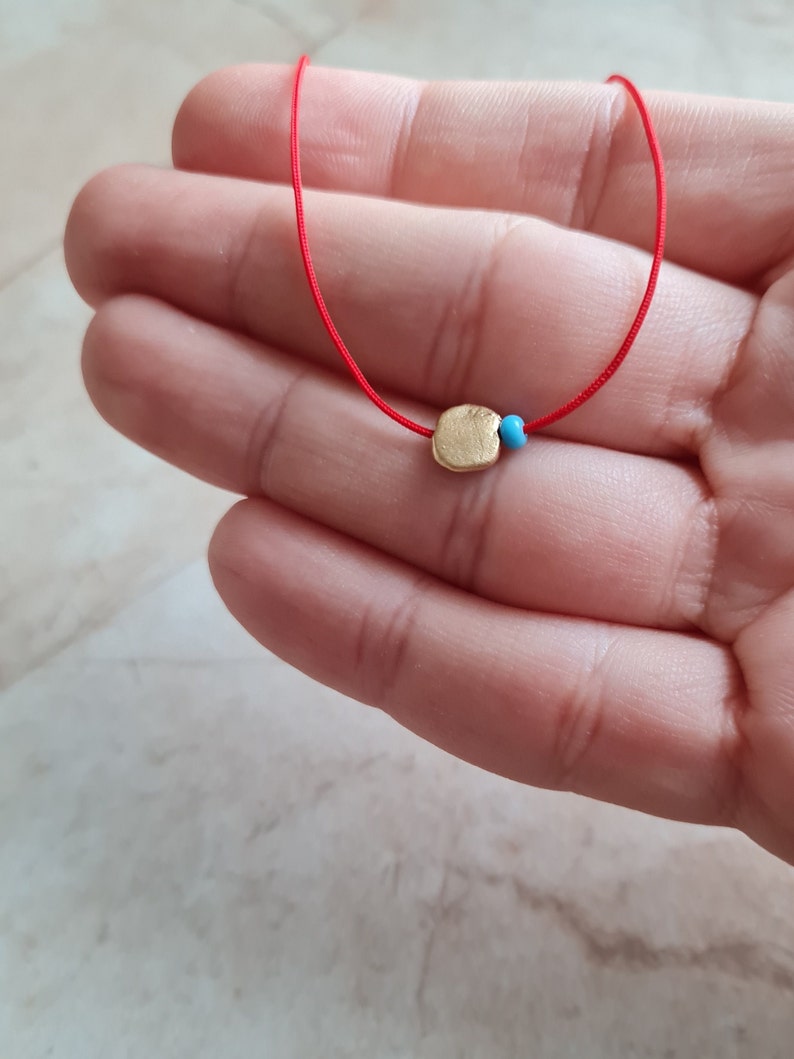 May include: A red string necklace with a gold charm and a blue bead.