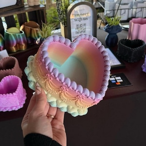May include: A pastel rainbow heart-shaped planter with a decorative scalloped edge. The planter is made of ceramic and has a smooth, glossy finish.