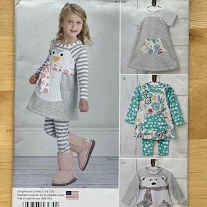 May include: Simplicity pattern 8270 features children's clothing designs. The pattern includes a dress with a penguin design, a dress with a pocket, and a top with a bear design. The pattern is designed and printed in the USA.