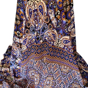 May include: A draped fabric with a detailed paisley pattern in shades of blue, brown, and cream. The fabric is arranged over a cylindrical form, showcasing the intricate design and color variations. The lower portion features a geometric border.