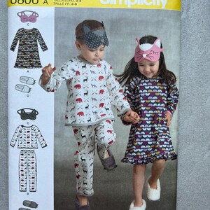May include: Simplicity sewing pattern 8806 for children's pyjamas and sleep masks. The envelope displays illustrations of a long-sleeve top, trousers, a nightgown, and animal-themed sleep masks with patterns featuring bears, deer, and arrows.