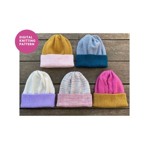 Könnte beinhalten: Sechs gestrickte Mützen in verschiedenen Farben, darunter Senfgelb, Teal, Hellblau, Weiß, Rosa und Lila. Die Mützen sind alle in der Hälfte gefaltet und auf einer Holzoberfläche ausgelegt. Der Text "DIGITAL KNITTING PATTERN" befindet sich in einem rosa Kreis in der oberen linken Ecke des Bildes.