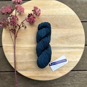 May include: A skein of dark blue yarn on a wooden surface with a tag that reads "150 Azul Profundo Chullo".