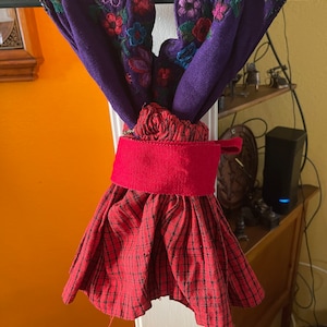 May include: A red and black plaid skirt with a red fabric waistband and a purple top with floral embroidery.