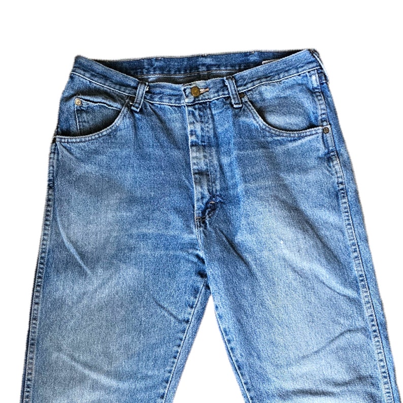 May include: A pair of blue denim jeans with a button fly and five pockets.