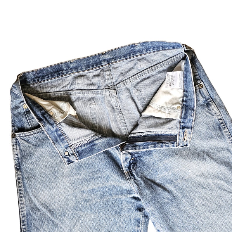 May include: A pair of light blue denim jeans with a button fly and a zipper. The jeans are turned inside out, showing the waistband and the inside of the pockets.
