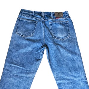 May include: A pair of blue denim jeans with a brown leather patch on the back waistband that says "Wrangler".