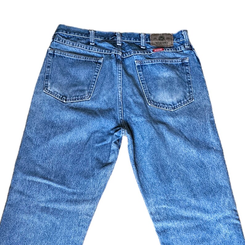 May include: A pair of blue denim jeans with a brown leather patch on the back waistband that says "Wrangler".