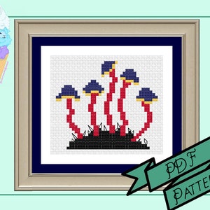 May include: Cross-stitch pattern of stylized mushrooms with red stems, blue caps, and yellow accents, set against a white background within a framed presentation. The frame is gold with a navy blue mat. A banner reads "PDF PATTERN".