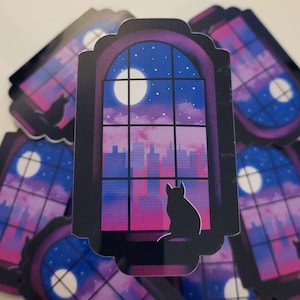 May include: A sticker featuring a black cat silhouette gazing out a window at a cityscape under a moonlit sky. The window frame is dark, and the sky transitions from blue to pink. Several stickers are visible.