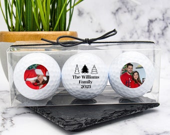 May include: Three white golf balls in a clear plastic box with a black ribbon. The golf balls are personalized with photos and the text "The Williams Family 2023".