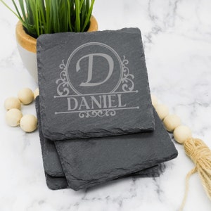 May include: Set of four black slate coasters with a monogrammed initial "D" and the name "DANIEL" engraved in a decorative font.