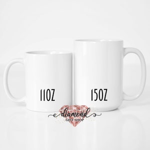 May include: Two white ceramic mugs with black text. The mug on the left says "11oz" and the mug on the right says "15oz".  A pink diamond logo with the text "diamond gift shop" is below the mugs.