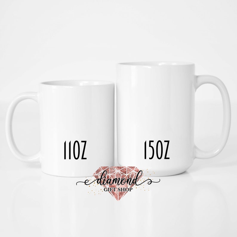 May include: Two white ceramic mugs with black text. The mug on the left says "11oz" and the mug on the right says "15oz".  A pink diamond logo with the text "diamond gift shop" is below the mugs.