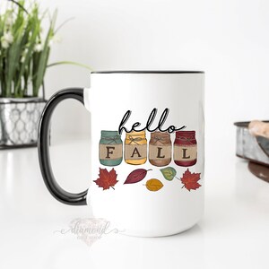 May include: White ceramic mug with a black handle. The mug has a design of four mason jars with the word "FALL" spelled out in the jars. The jars are decorated with burlap and twine. The text "hello" is written above the jars. There are also fall leaves around the jars.