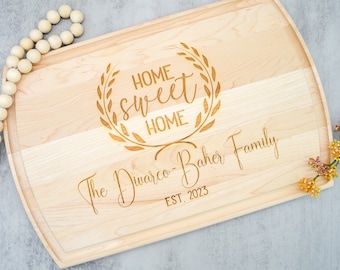 May include: A wooden cutting board with a decorative engraved design that says "Home Sweet Home" with a laurel wreath around the text. The board also has the text "The Diwarco-Baker Family Est. 2023" engraved on it.