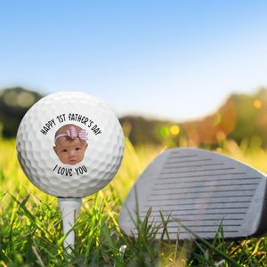 Pu&ograve; includere: Una palla da golf bianca con il viso di un bambino e il testo "Happy 1st Father's Day I Love You" stampato su di essa.