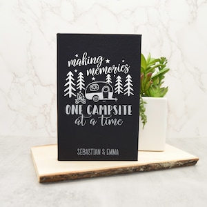 May include: Black canvas sign with white text and a camper silhouette. The text reads "making memories one campsite at a time" with the names "Sebastian & Emma" at the bottom.