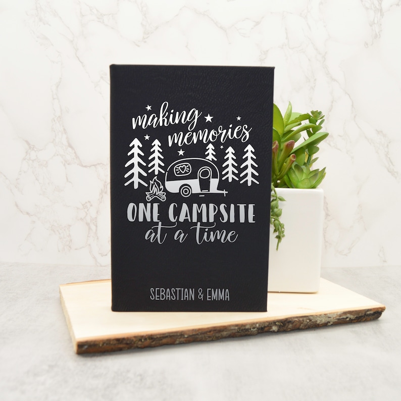 May include: Black canvas sign with white text and a camper silhouette. The text reads "making memories one campsite at a time" with the names "Sebastian & Emma" at the bottom.