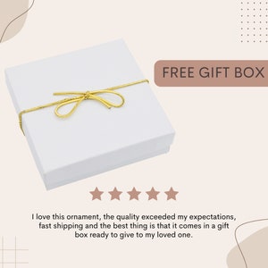 May include: A white gift box with a gold ribbon tied in a bow. The box is sitting on a white surface. The text "FREE GIFT BOX" is written in brown letters on a light brown background.
