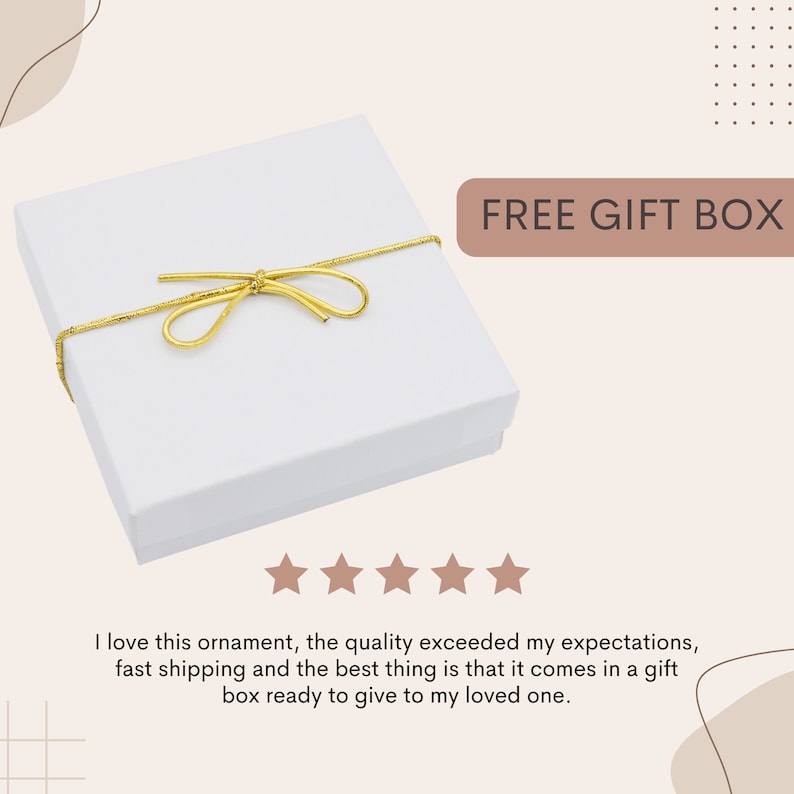 May include: A white gift box with a gold ribbon tied in a bow. The box is sitting on a white surface. The text "FREE GIFT BOX" is written in brown letters on a light brown background.