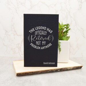 May include: Black leather journal with the text "The Legend Has Officially (Retired) Not My Problem Anymore" and the name "David Johnson" engraved on the front.