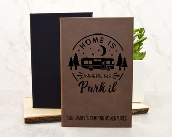 May include: Brown leather-bound journal with a black design of a camper van, trees, stars, and a crescent moon. The text reads "Home is where we park it" and "Our family's camping adventures".